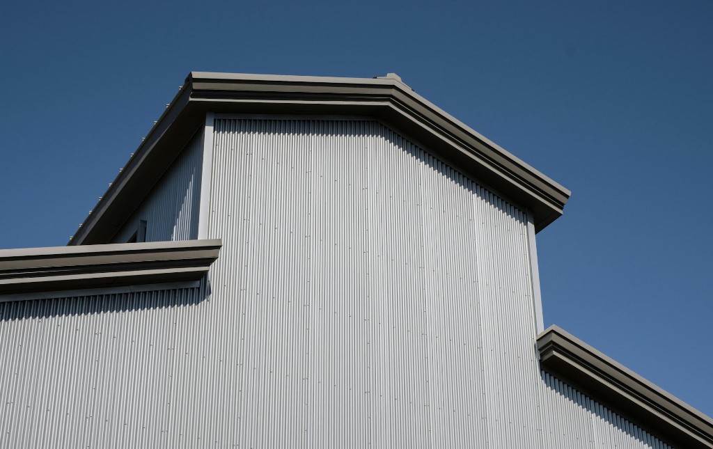 Dark bronze seamless gutters along a modern home with light corrugated metal siding against a clear blue sky