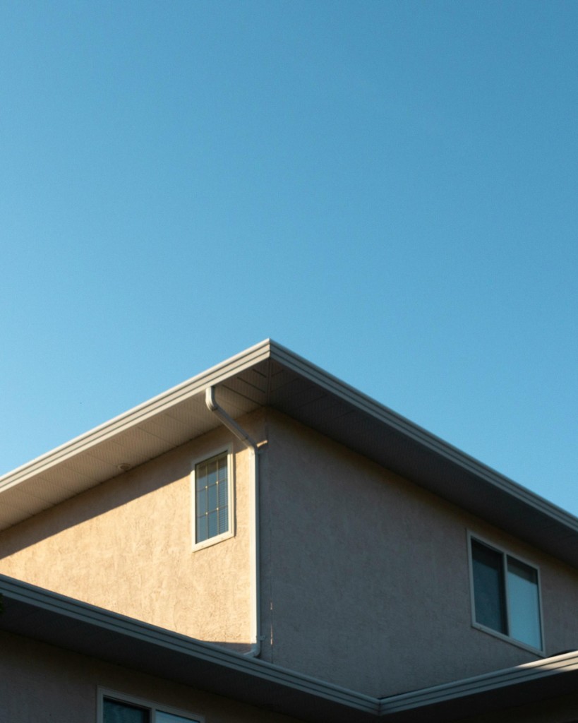 White seamless gutters and downspout on a beige stucco home under a clear blue sky