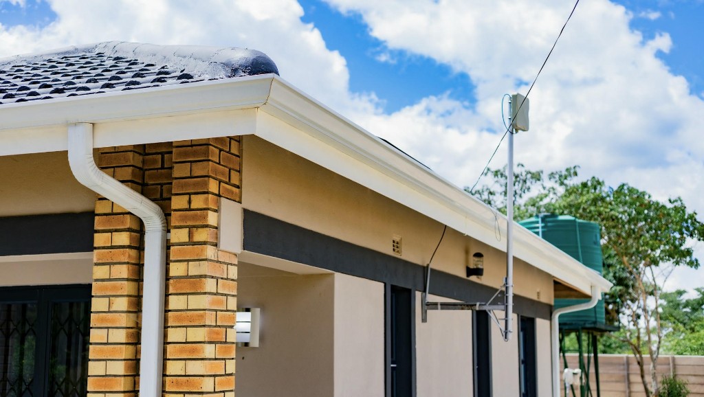 White gutters and downspouts along the roofline of a home with brick columns and a blue sky