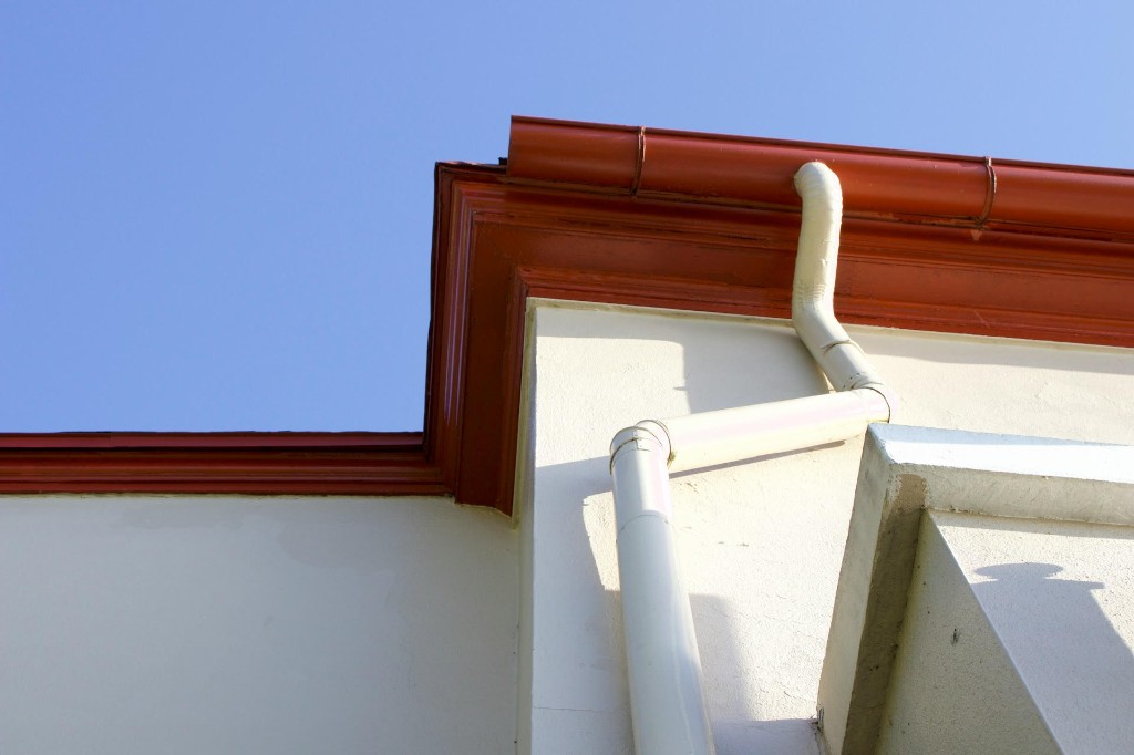 Terracotta gutter and cream downspout on a bright blue-sky roofline