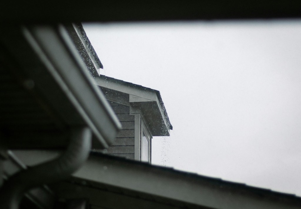 Rainwater pouring off a roof edge without adequate gutter coverage during a storm