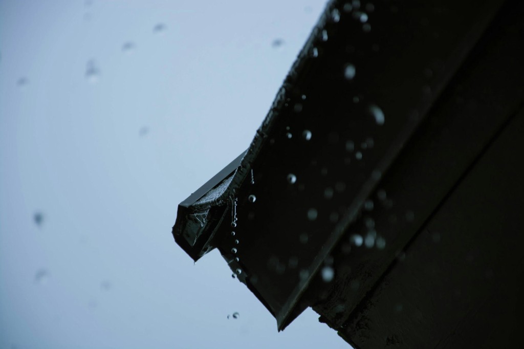 Rain dripping from a dark gutter end cap against an overcast sky