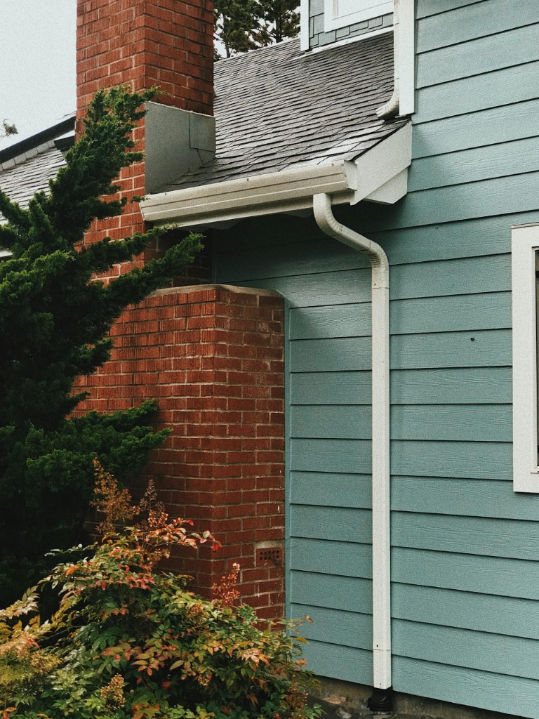 White gutters and downspouts on a new home with blue-grey siding, dark shingles, and a red brick chimney