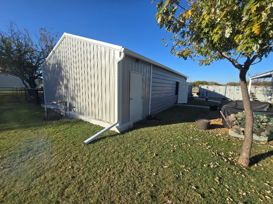 White gutters and downspout extension on an Allen metal shed