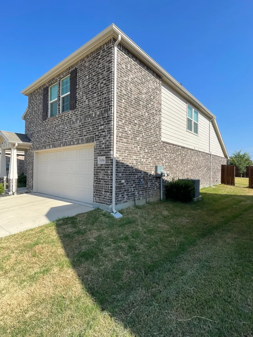 White gutters on a two-story brick home with tan siding in Dallas