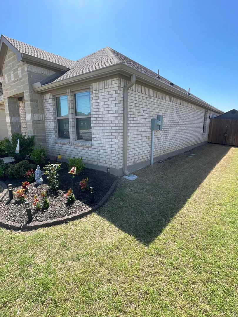 Tan gutters on a brick home with landscaping in North Texas