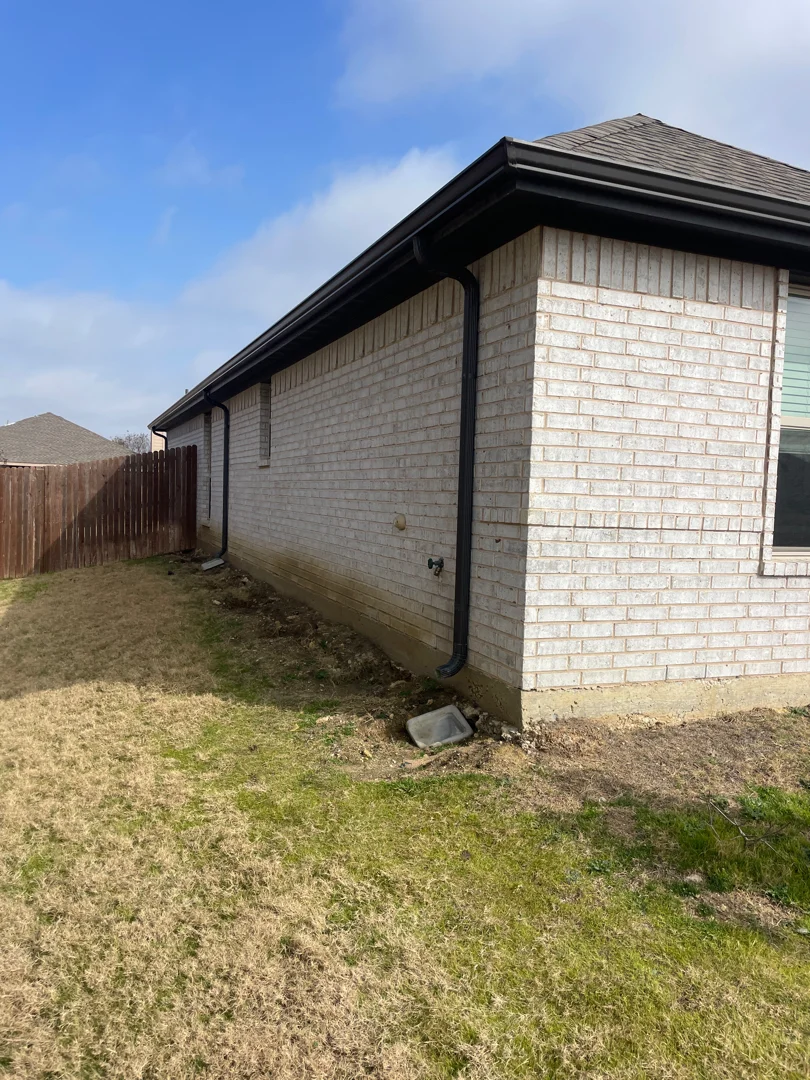 Cream brick Plano home with dual black downspouts and gutters